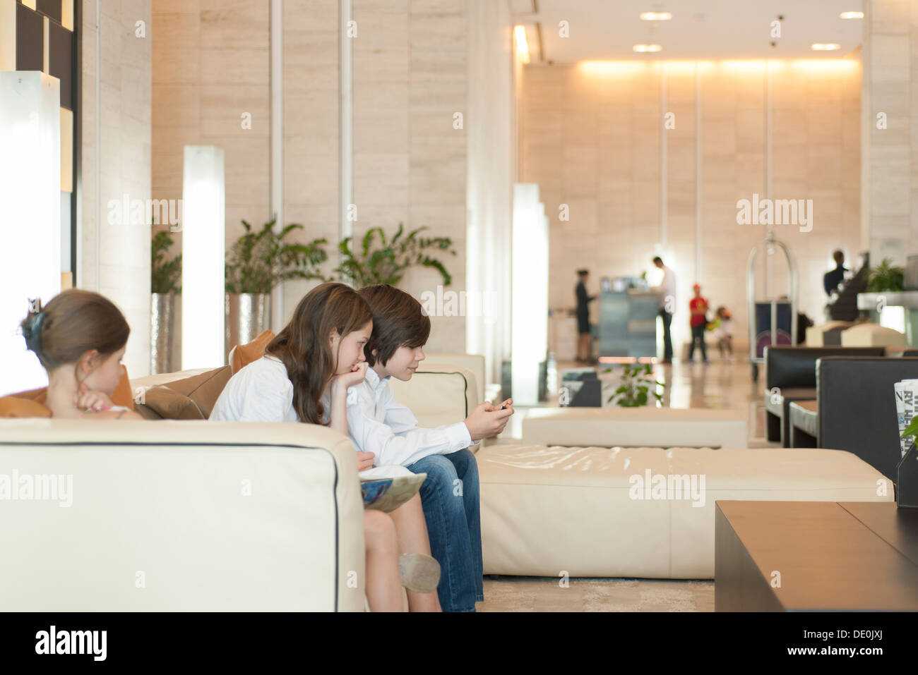 Les jeunes frères et sœurs en utilisant smartphone dans hall de l'hôtel Banque D'Images