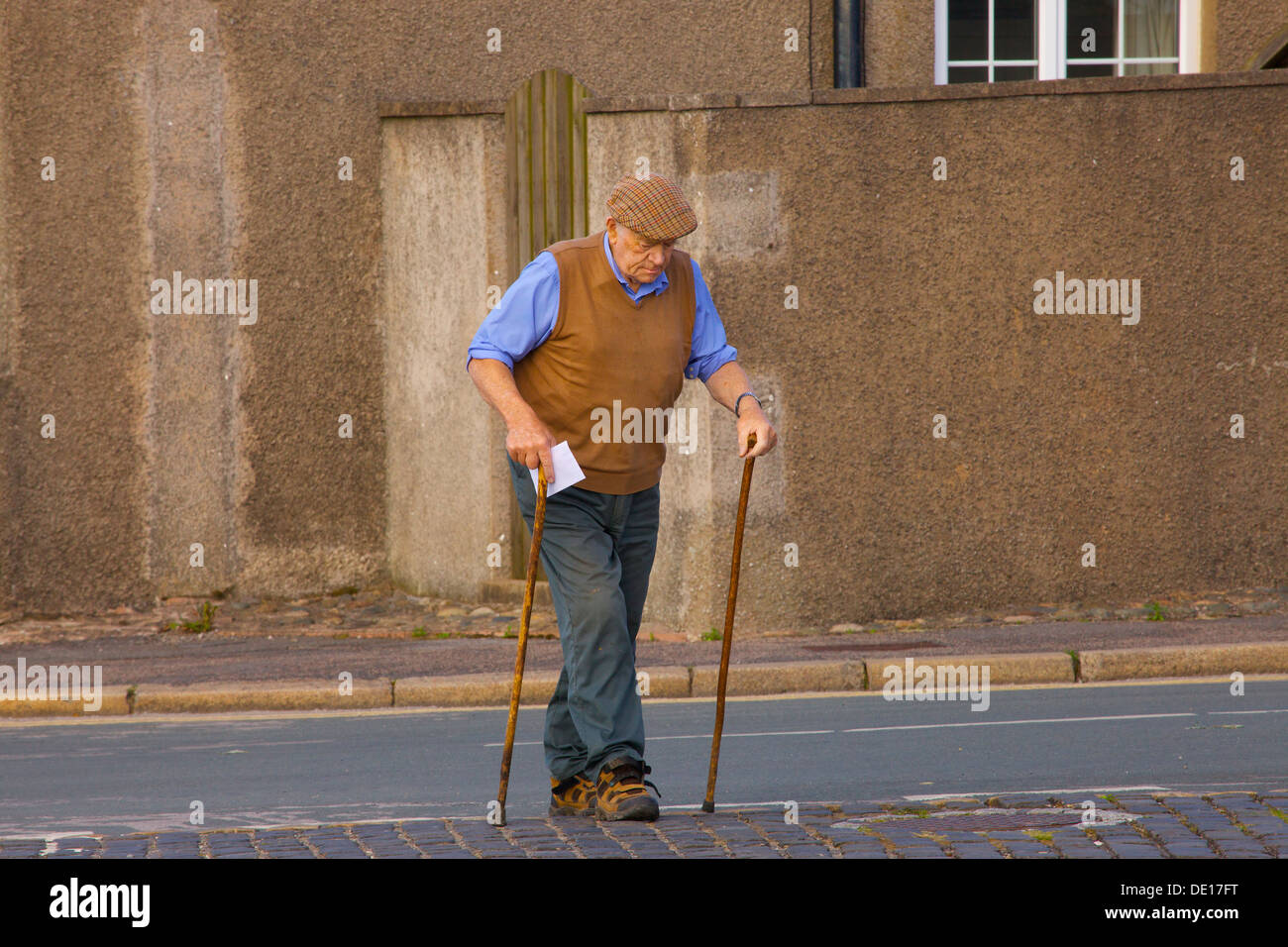 Vieil homme avec les bâtons de marche, traversant la rue pour poster une lettre. Le nord de l'Angleterre. Banque D'Images