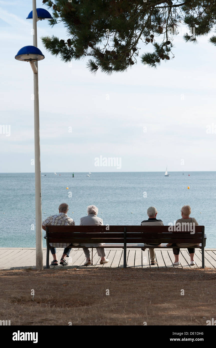 Vue arrière de quatre personnes âgées assises sur un banc au bord de la mer à Benodet Bretagne France Banque D'Images