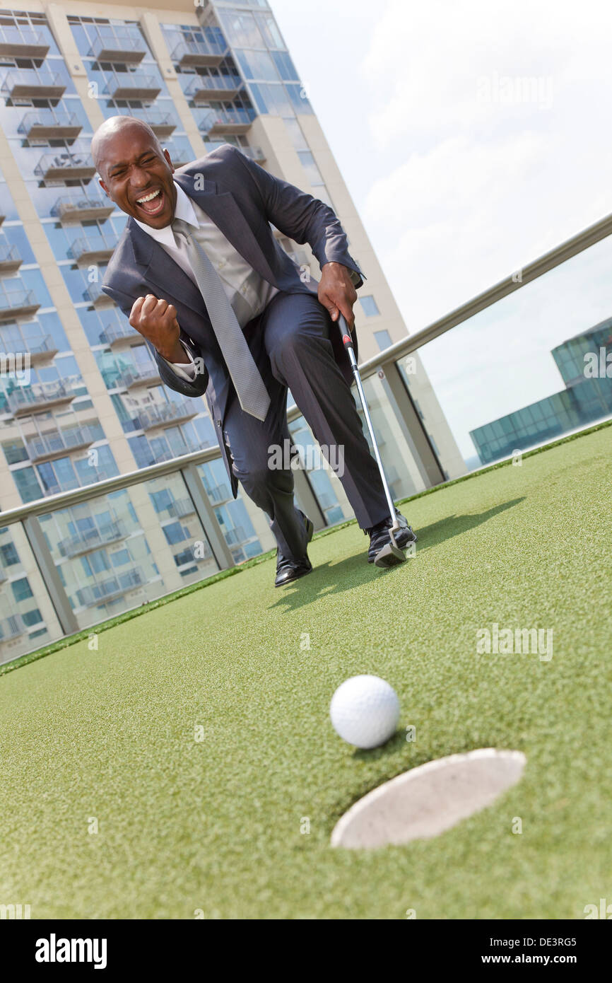 African American businessman ou homme en costume en jouant au golf sur un putting green sur le toit d'un gratte-ciel office building Banque D'Images
