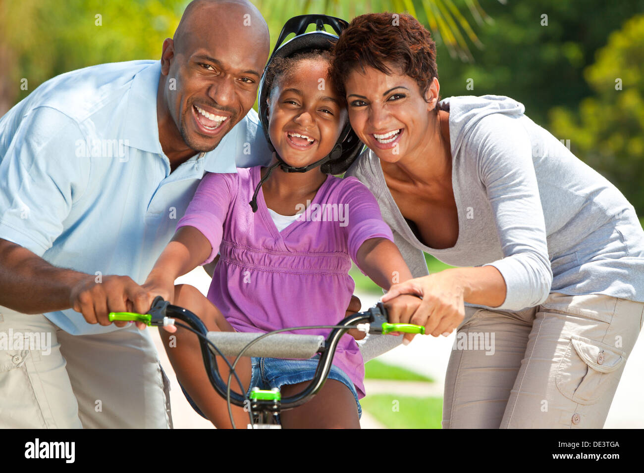 Un jeune African American family with girl child riding son vélo et ses heureux parents excité l'encouragement à côté d'elle Banque D'Images