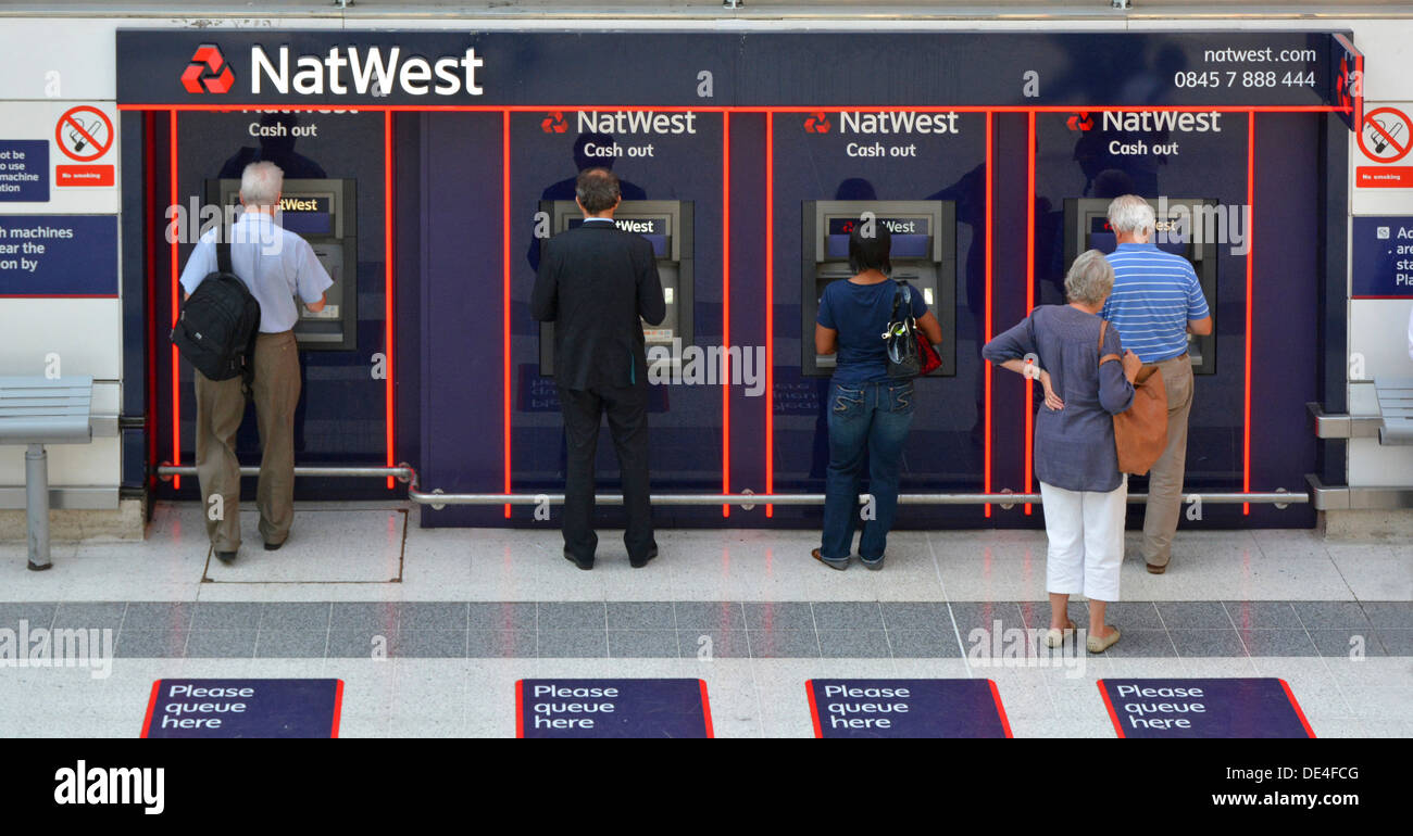 Vue arrière des personnes utilisant ou attendant à tous les quatre NAT West Bank retrait ATM trou dans les machines murales à l'intérieur de la gare de Londres Angleterre Royaume-Uni Banque D'Images
