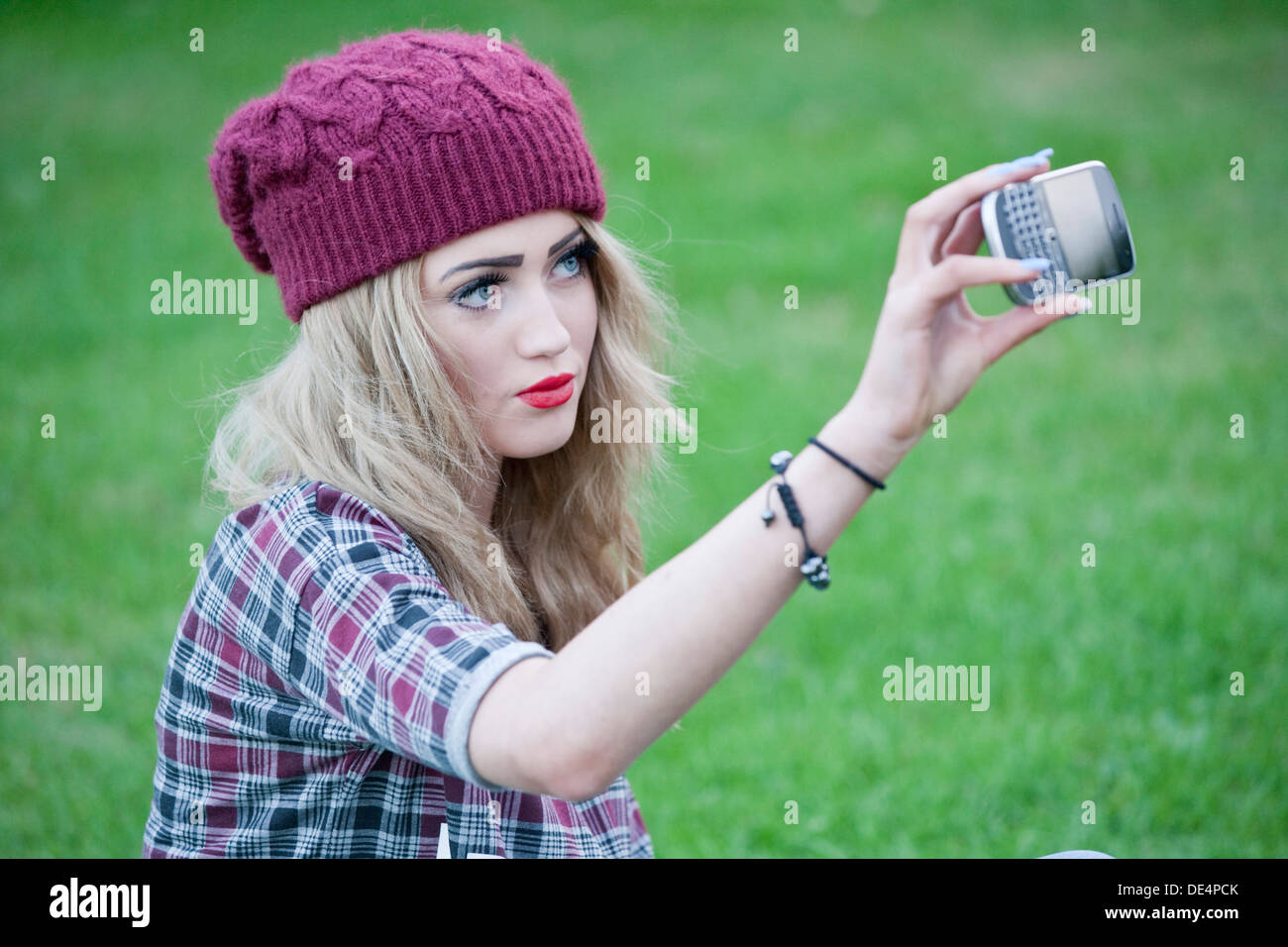 Adolescente blonde assis dehors prendre un autoportrait sur son téléphone. Banque D'Images