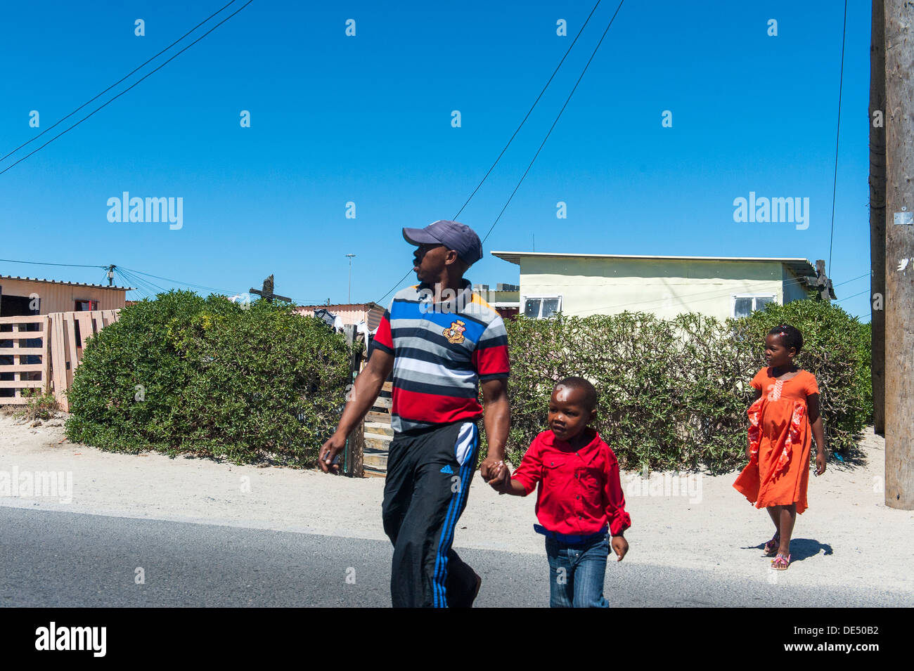 Le père et les enfants traversant une route à Khayelitsha, un township informel partiellement à Cape Town, Western Cape, Afrique du Sud Banque D'Images