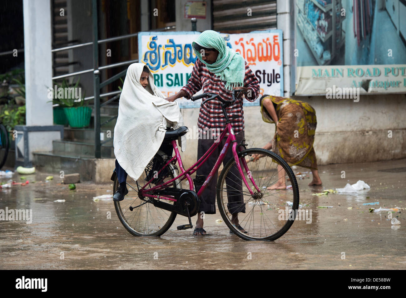 Père et fils se indien sur une bicyclette sous la pluie. Puttaparthi, Andhra Pradesh, Inde Banque D'Images