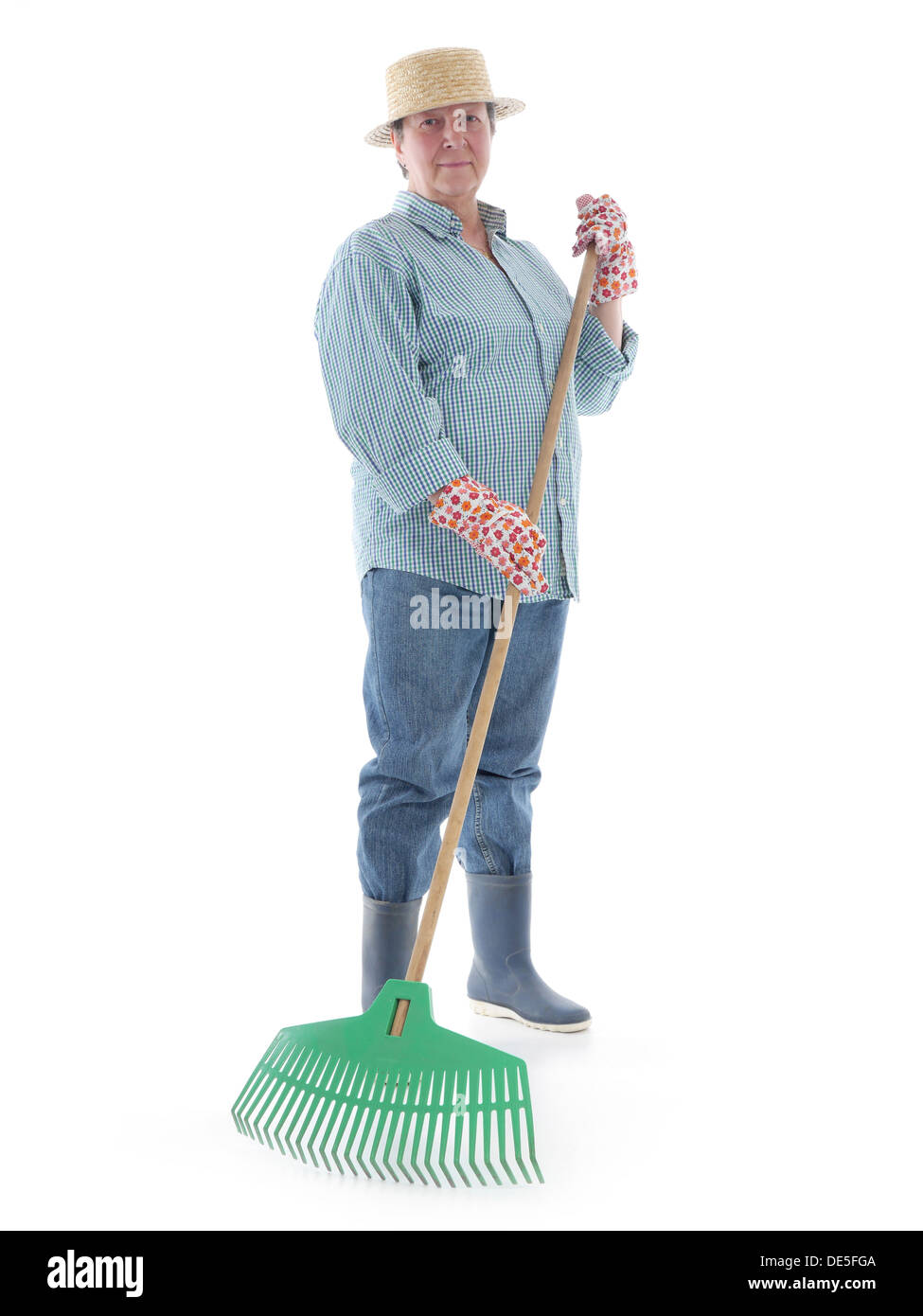 Jardinier Senior woman wearing straw hat et des bottes en caoutchouc posant avec un râteau de jardin en plastique sur fond blanc Banque D'Images