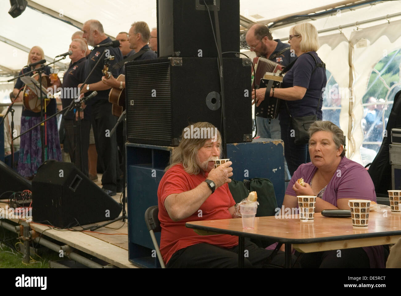 Couple de tente de bière mangeant et buvant des tasses de thé d'une tasse de papier. Le groupe folk est Friggn Riggin. Widecombe Fair, Widecombe in the Moor, Dartmoor, Devon UK. HOMER SYKES Banque D'Images