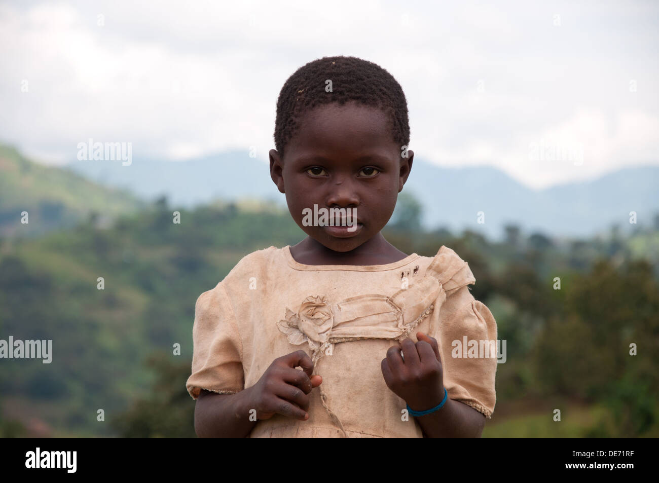 Jeune fille ougandaise avec montagnes en arrière-plan à la caméra en portant des vêtements en lambeaux Banque D'Images