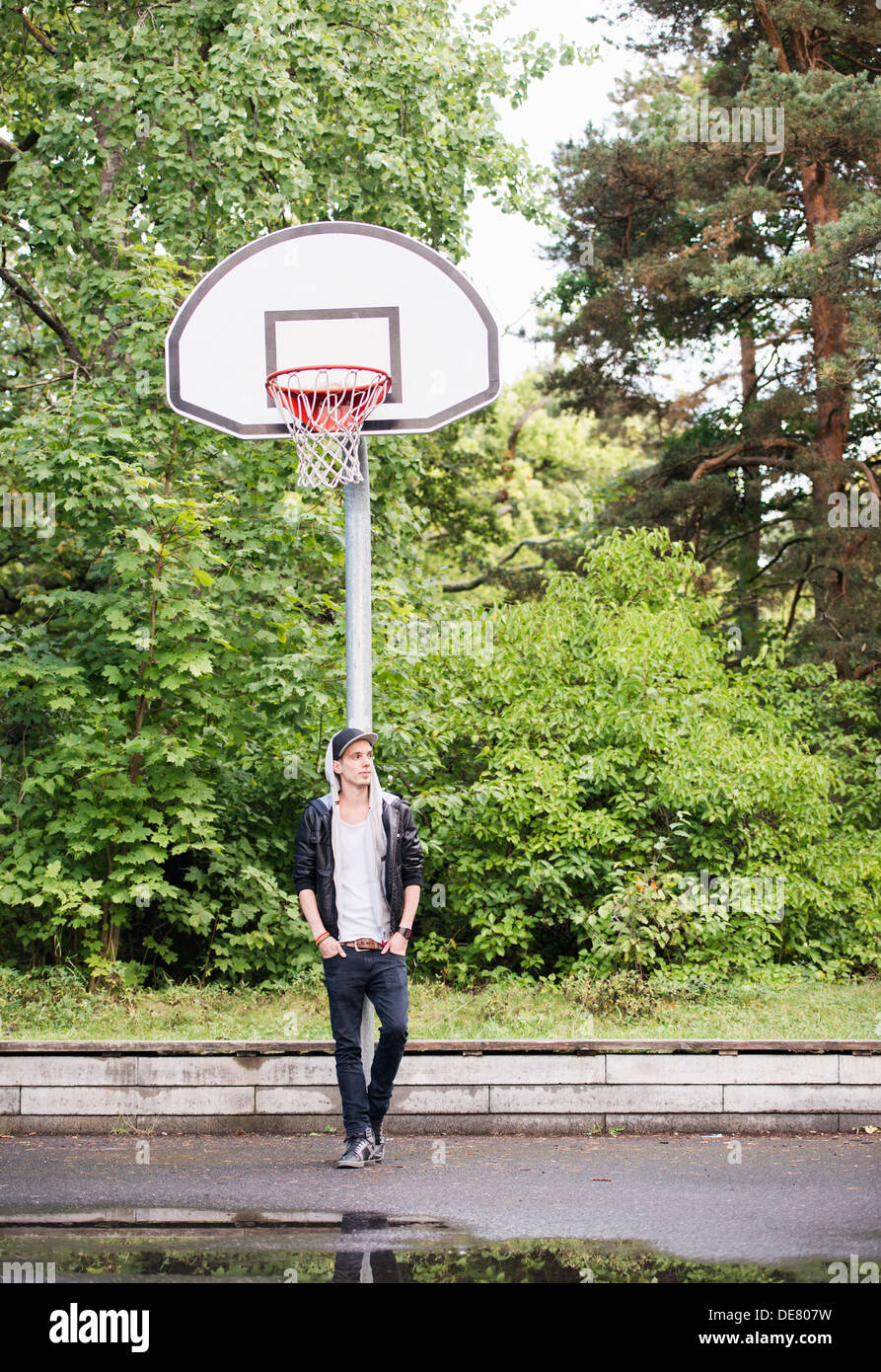 Portrait de vie de jeune homme en veste de cuir en attente à un terrain de basket-ball extérieur Banque D'Images