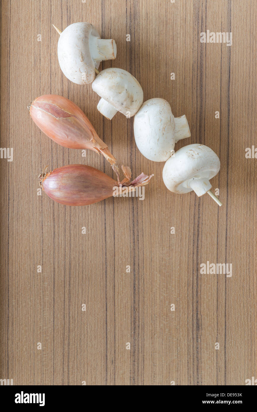 Champignons frais et les échalotes sur un comptoir de cuisine en bois en attente d'être utilisés comme ingrédients dans la cuisine savoureuse Banque D'Images