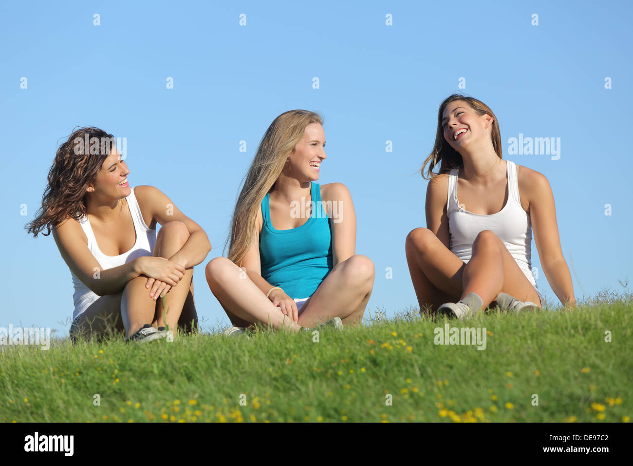 Groupe de trois adolescentes rire et parler dans l'herbe avec le ciel en arrière-plan Banque D'Images