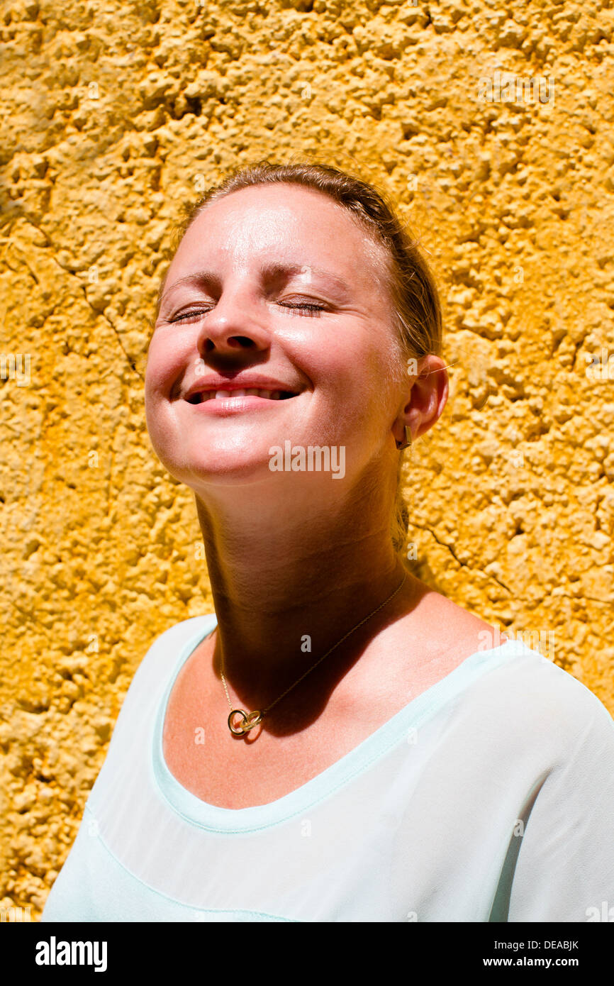 Girl Enjoying the Sun en face d'un mur jaune Banque D'Images