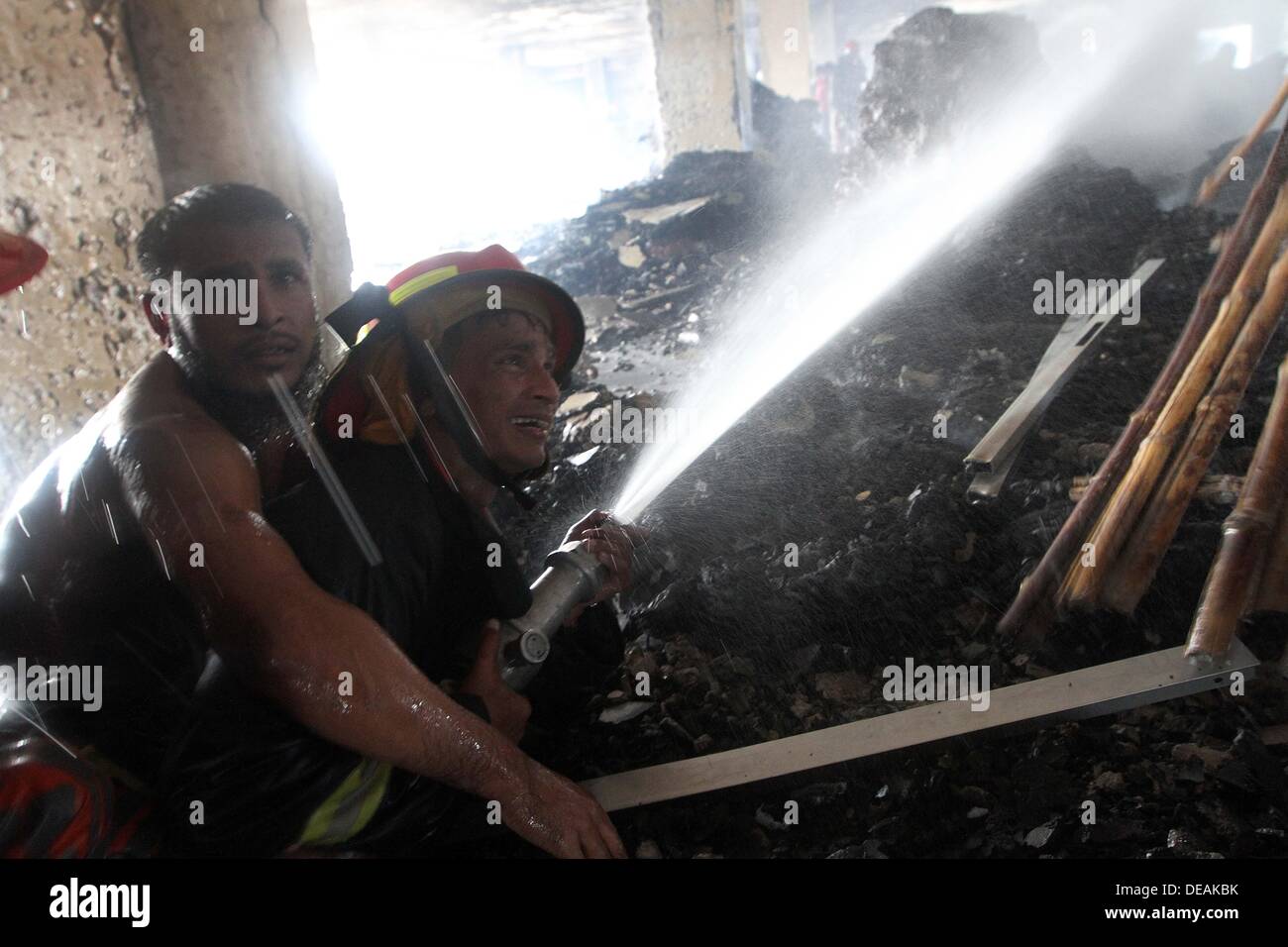 Pompier avec l'aide de jeunes locaux à partir d'une distance de l'eau sur un brasier pulvérisations durant un incendie dans une usine de vêtements à Dhaka le 15 septembre 2013. Aucune victime n'a été signalée à partir de l'incendie à la Sicile de six étages de l'usine de vêtements. Le Bangladesh, le deuxième plus grand exportateur de vêtements avec ses usines de vêtements représentant 80 pour cent de ses expéditions outre-mer, a été frappé par une série de catastrophes récentes mettant en lumière des conditions de sécurité effroyables à de nombreuses usines Banque D'Images