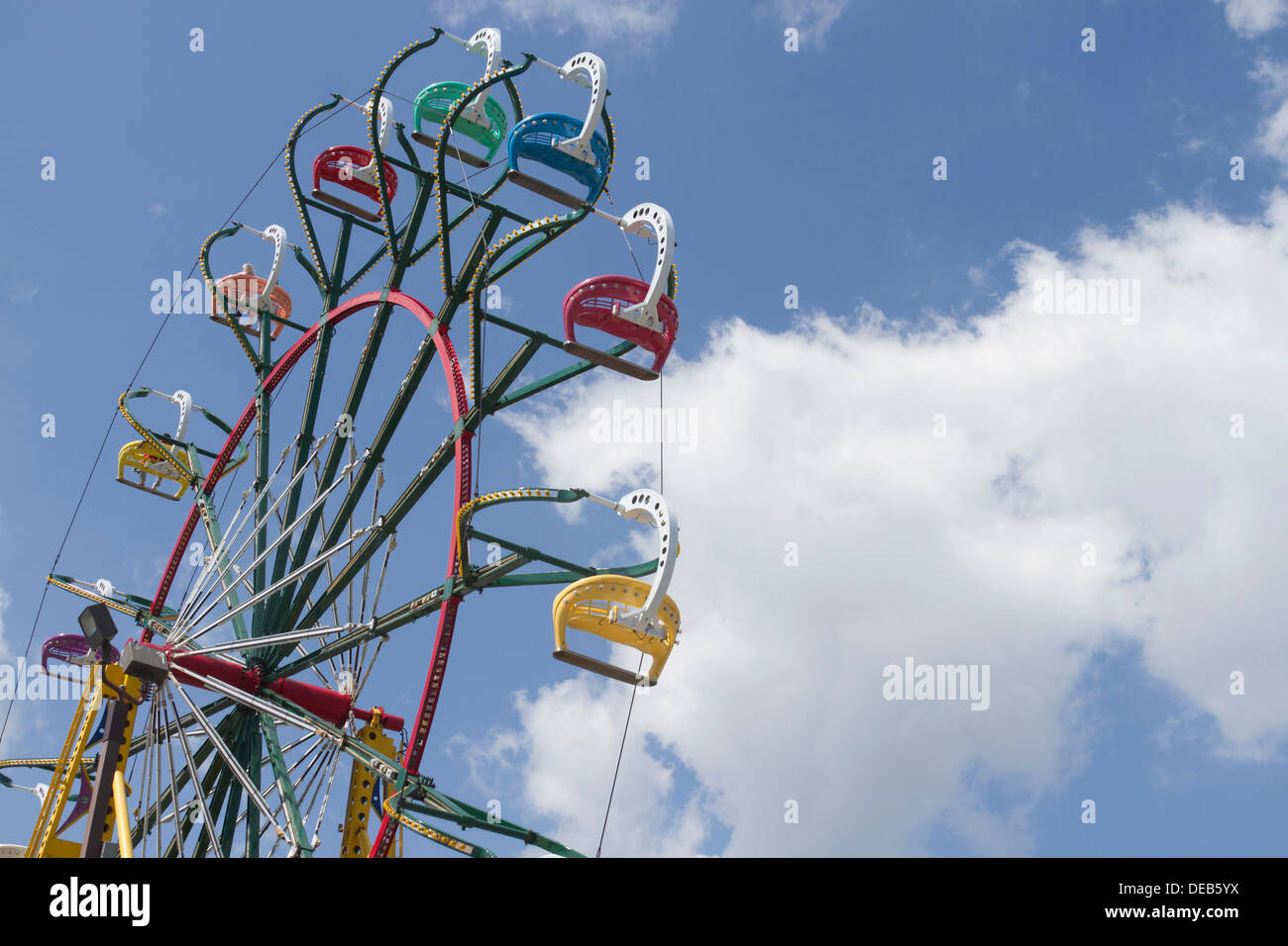 Les gens monter une roue de Ferris, coloré en contraste frappant contre un ciel bleu profond avec puffy nuages blancs à l'État juste à Nort Banque D'Images