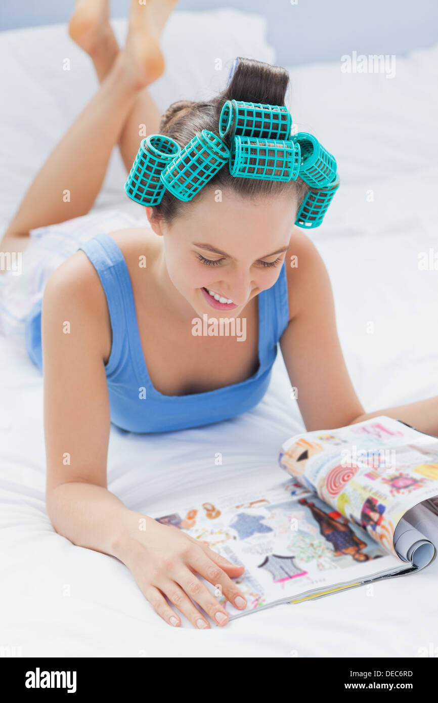 Smiling girl in hair rollers lying on bed Banque D'Images