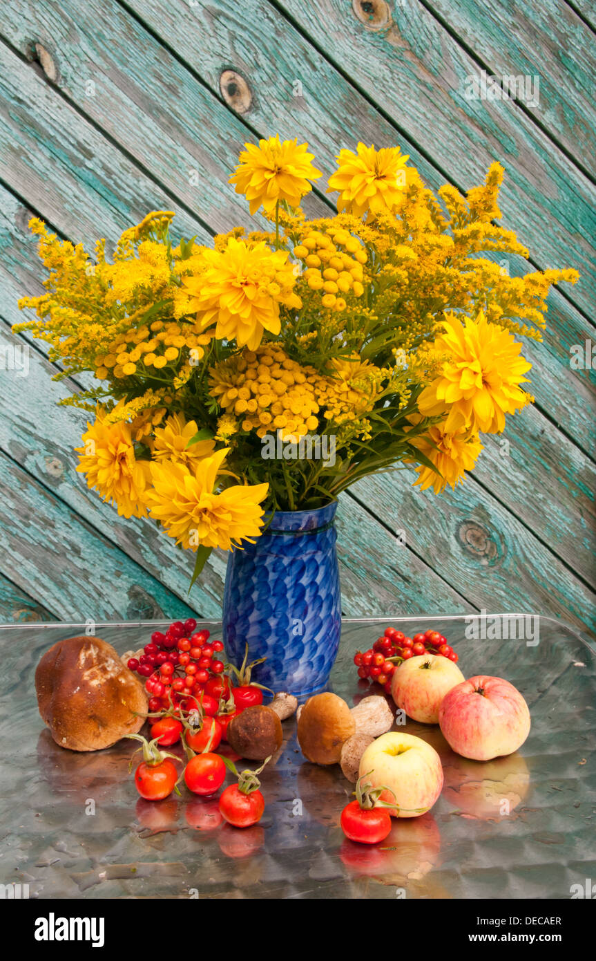 Bouquet de fleurs jaunes dans un vase bleu avec des pommes et rose-hanches Banque D'Images