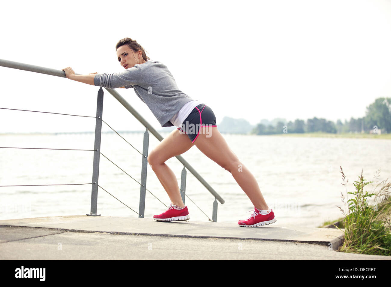 Coureuse en bonne santé s'étend pendant la course ou le jogging piscine d'entraînement. Le port de vêtements de conditionnement physique. Banque D'Images