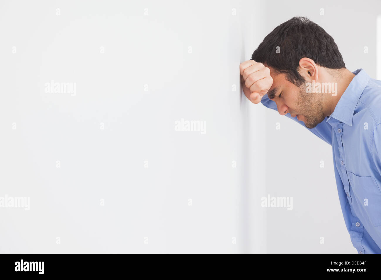 Homme en colère posant sa tête contre un mur Banque D'Images