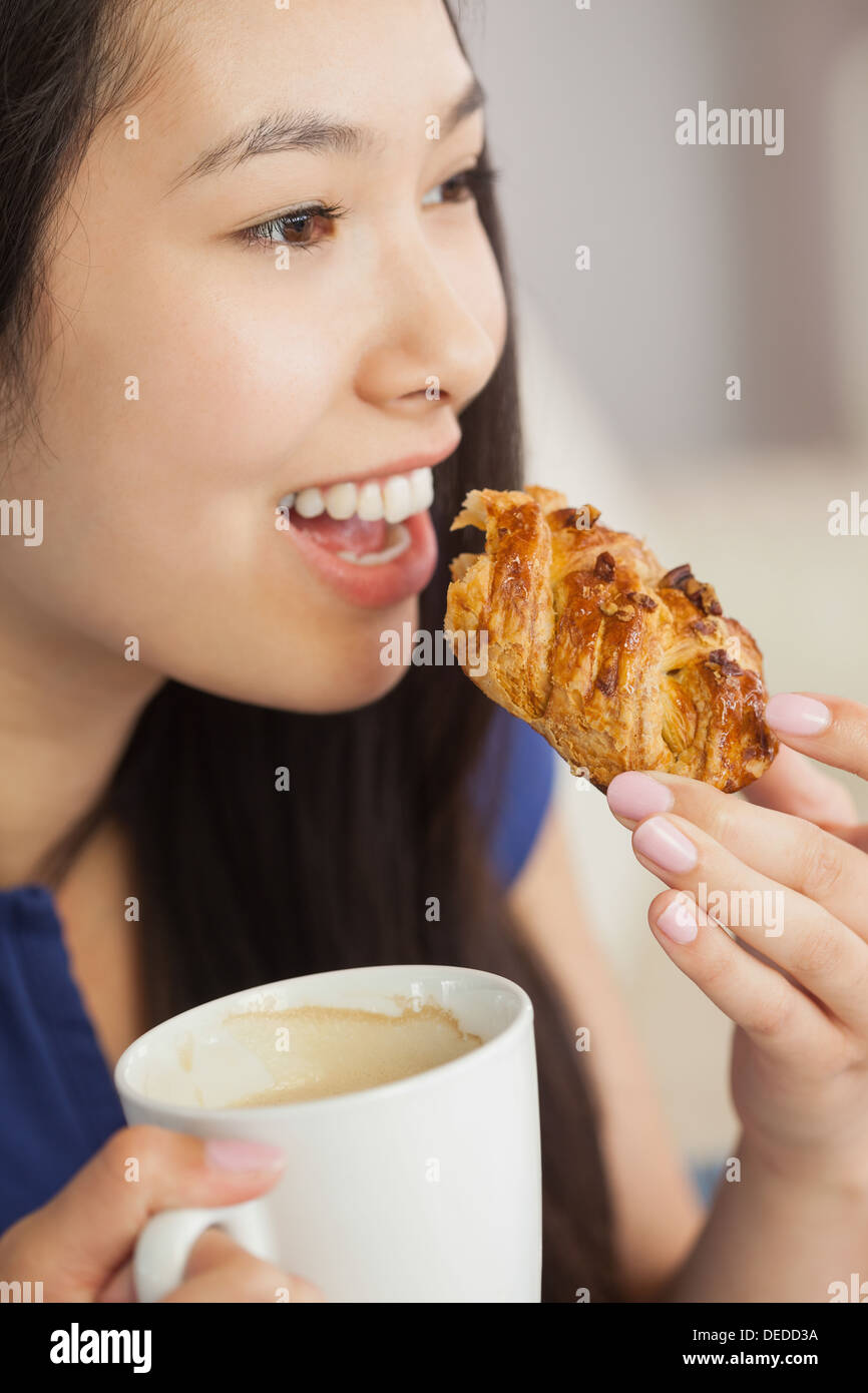 Young Asian woman eating une pâtisserie avec une tasse de café Banque D'Images