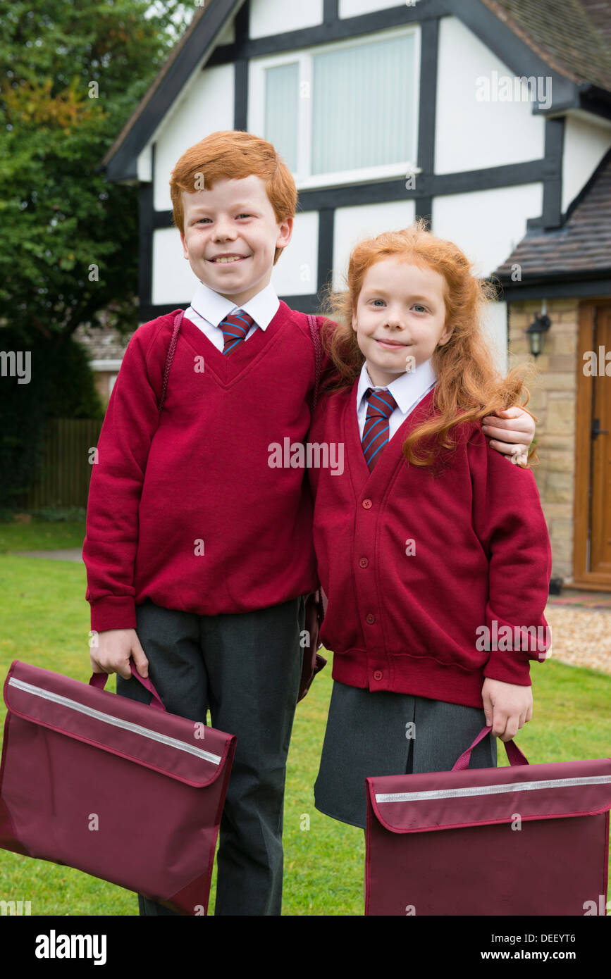 Frère et soeur dans leur uniforme de l'école à l'extérieur de leur maison. Banque D'Images