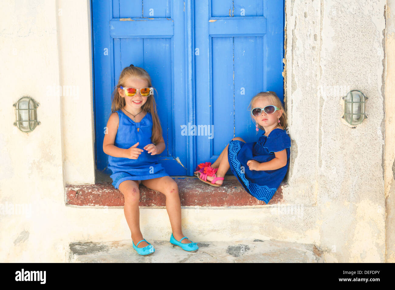 Cute Little Sisters sitting près de la vieille porte bleue dans village grec d'Emporio, Santorin Banque D'Images