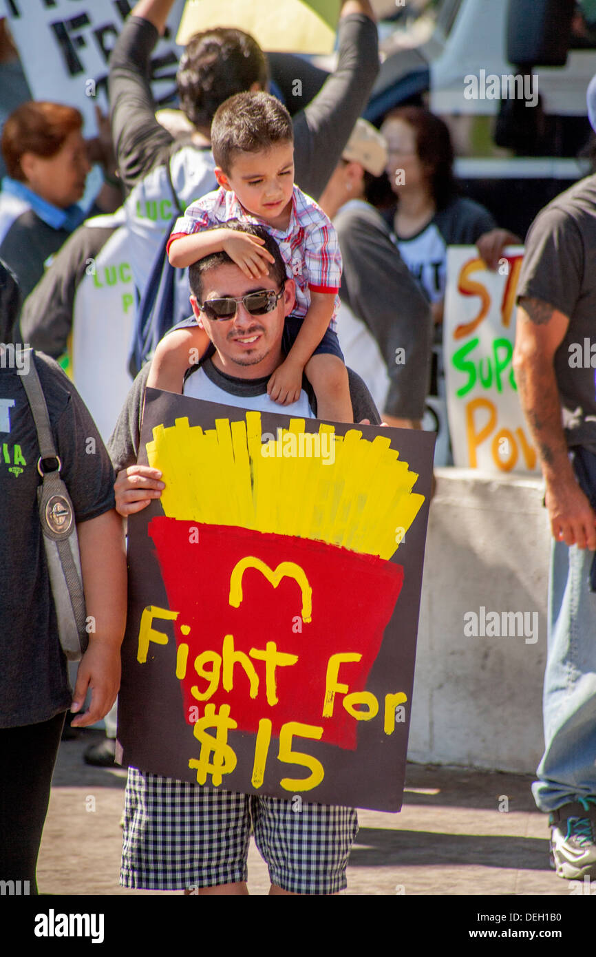 Avec un panneau d'un MacDonald's portion de frites avec un salaire horaire de 15 $, la demande d'un père d'origine hispanique se joint à une manifestation. Banque D'Images