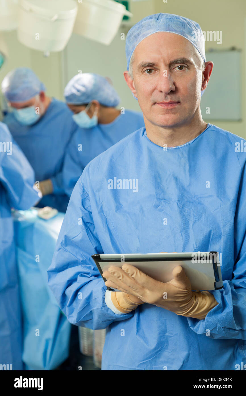 Hauts homme médecin chirurgien à l'aide de l'ordinateur tablette avec l'équipe chirurgicale interracial et patient en salle d'opération de l'hôpital Banque D'Images