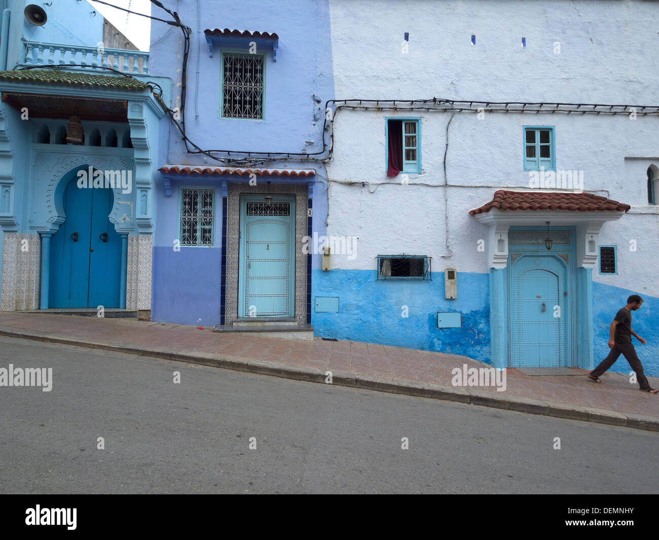 Homme marchant par les maisons peintes en bleu clair à Chefchaouen, Maroc Banque D'Images
