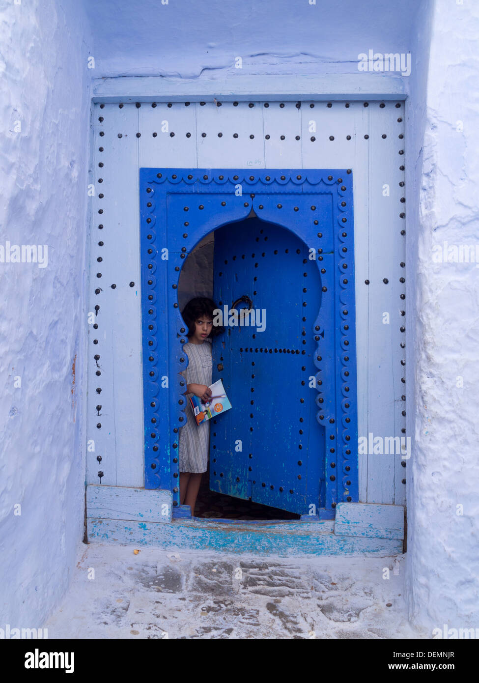 Jeune fille sur l'entrée de porte avec porte ouverte, Chefchaouen, Maroc Banque D'Images