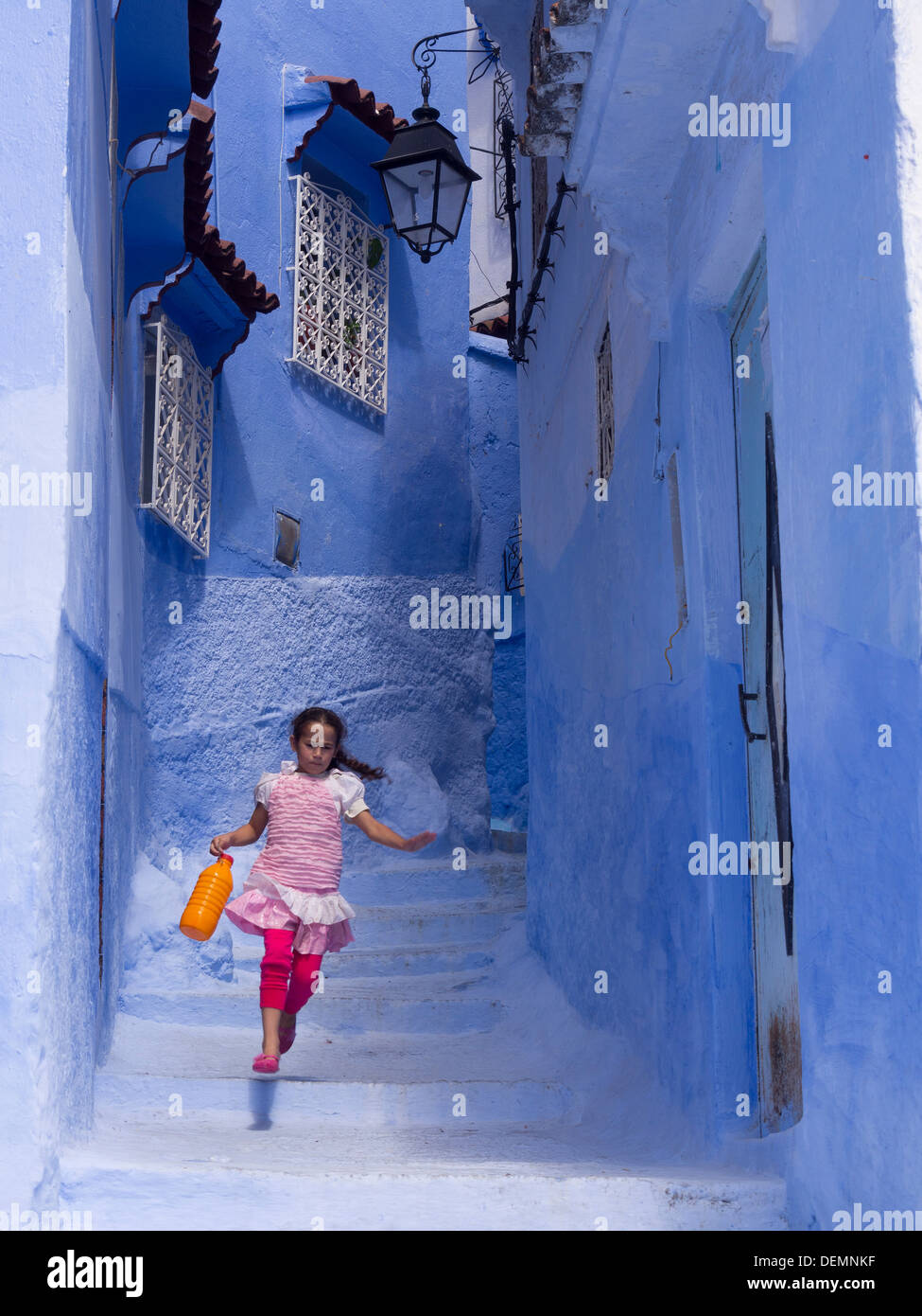 Jeune fille courir dans la rue avec des maisons peintes en bleu clair à Chefchaouen, Maroc Banque D'Images
