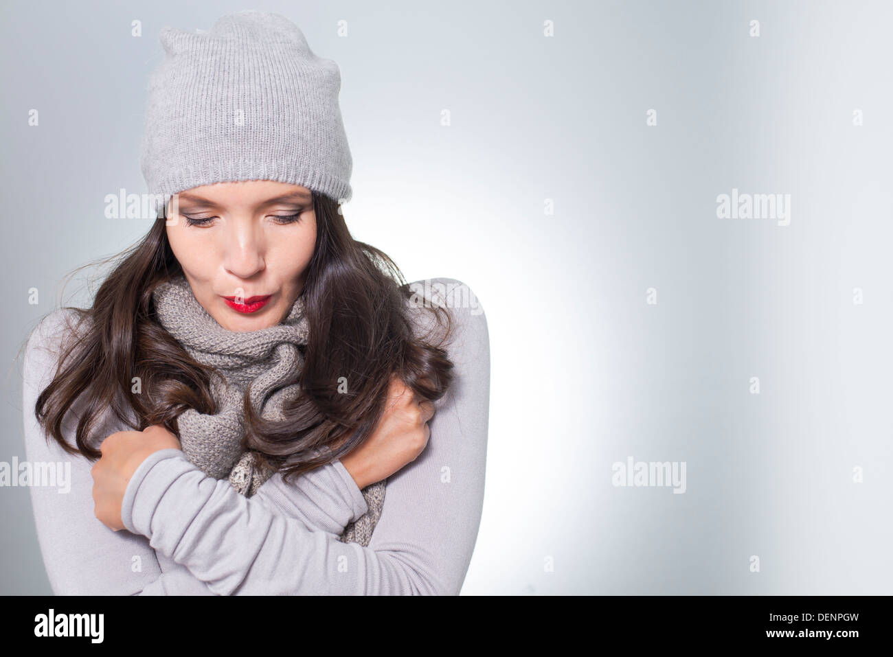 Jolie jeune femme en hiver la mode câlins à l'intérieur de son tricot jersey laineux gris, écharpe et cap sur une journée froide Banque D'Images