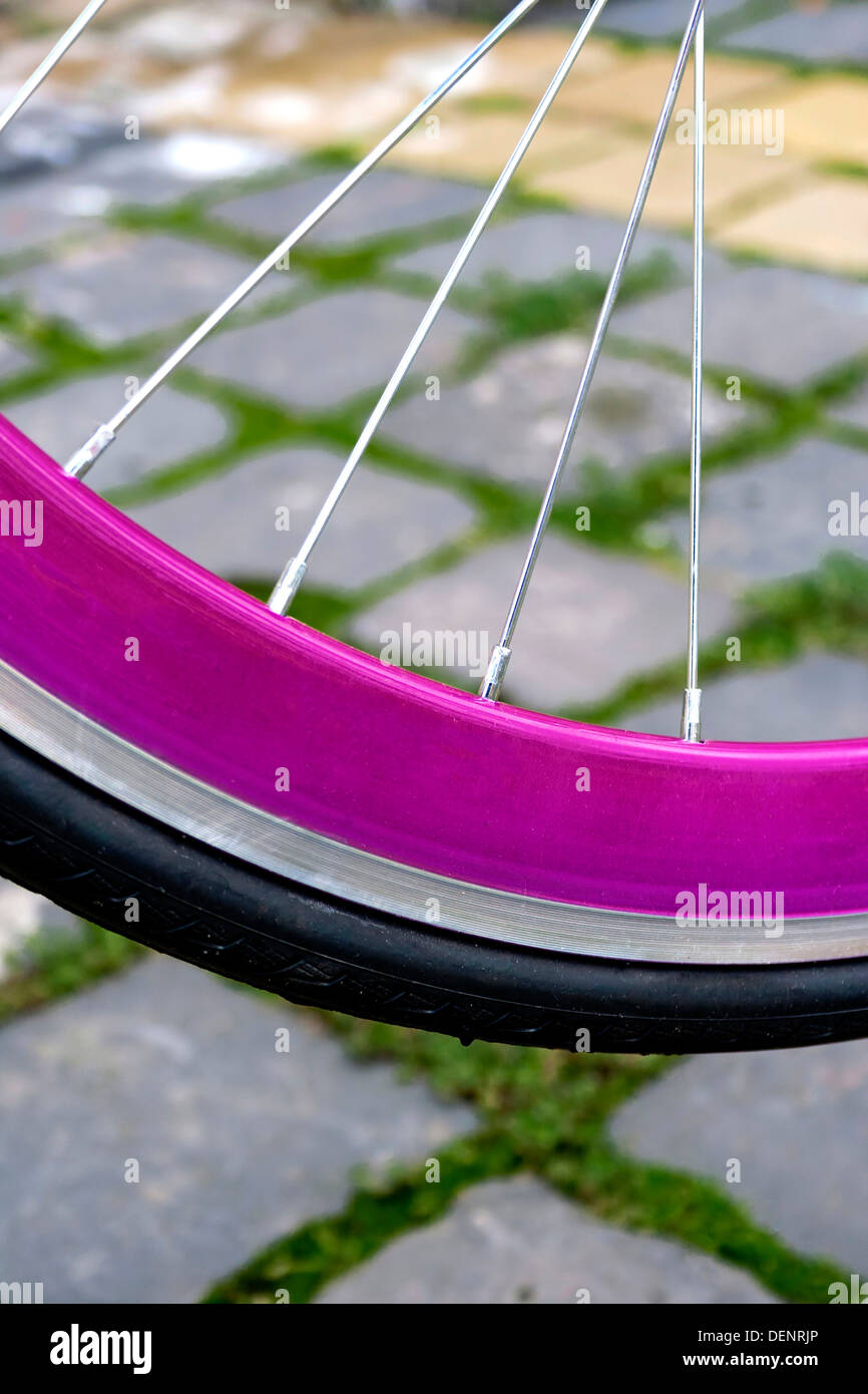 Détail d'une roue de vélo en caoutchouc, avec jante rose, sur un pavage. Banque D'Images