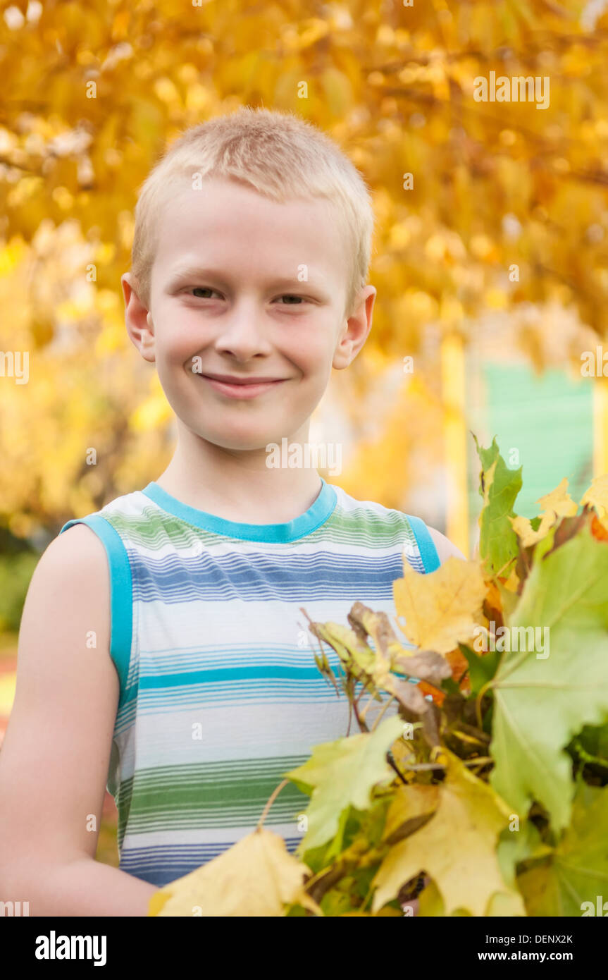 Adorable boy smiling and holding les feuilles d'automne au cour de l'école Banque D'Images