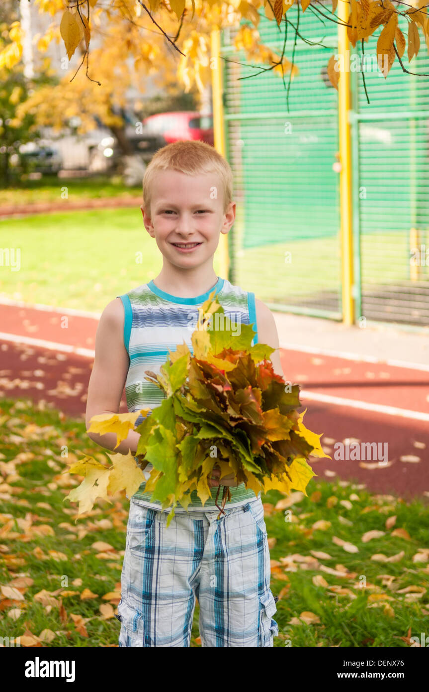 Adorable boy smiling, feuilles d'automne sur un terrain d'école Banque D'Images