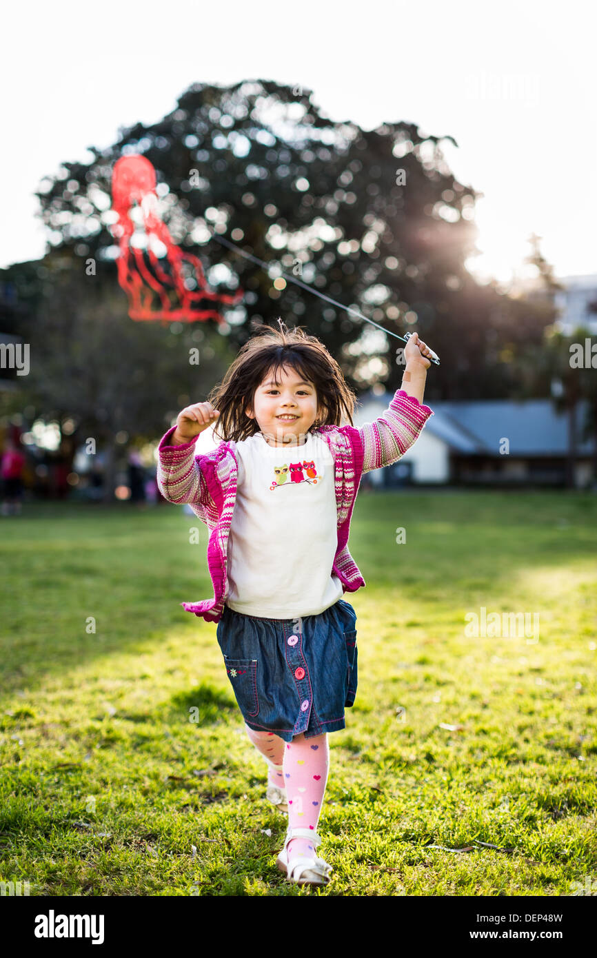 Jeune fille courir vers l'appareil photo volant un cerf-volant Banque D'Images