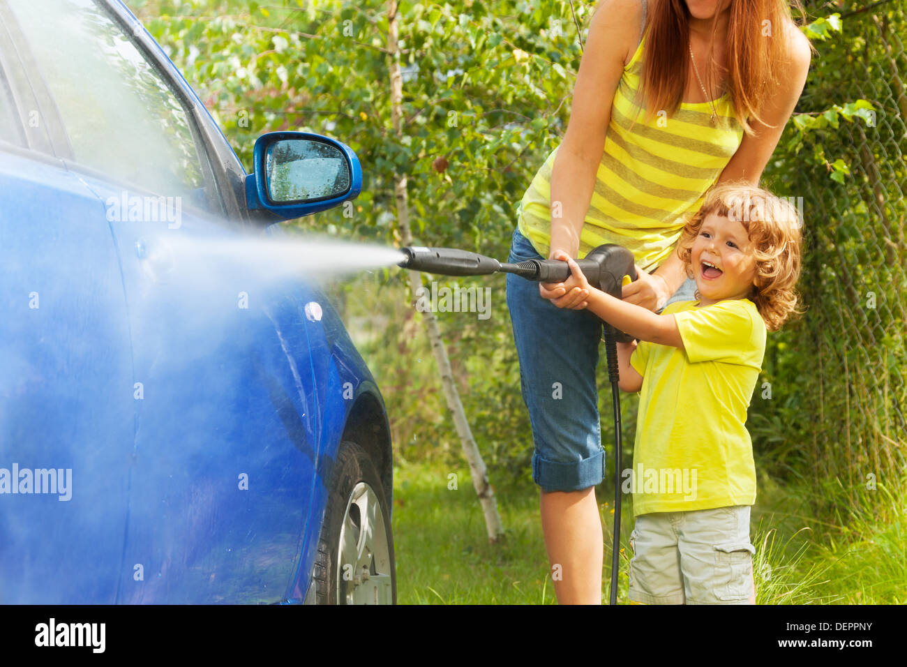 Mère et son fils de trois ans avec voiture lavage laveuse à haute pression avec buse de pointage garçon debout dans l'eau à l'extérieur dans le parking ans dormant Banque D'Images