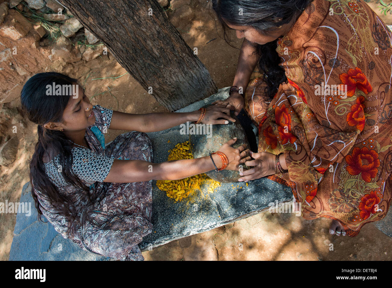 Deux femmes indiennes curcuma poudre de racines de broyage avec une pierre ronde dans un village de l'Inde rurale. L'Andhra Pradesh, Inde Banque D'Images