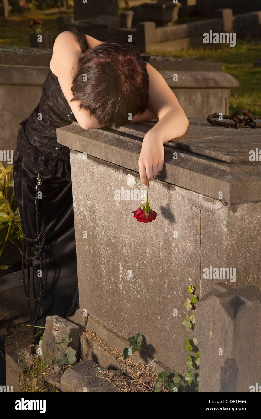 Crying Girl gothique appuyée sur une pierre tombale tenant une rose Banque D'Images