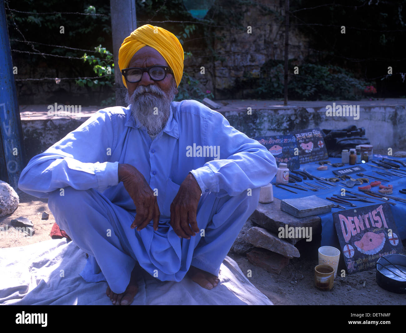 Personnes âgées (homme) dentiste avec couleur safran turban, accroupis dans street à Jaipur, Rajasthan, Inde. Outils de son surround du commerce Banque D'Images