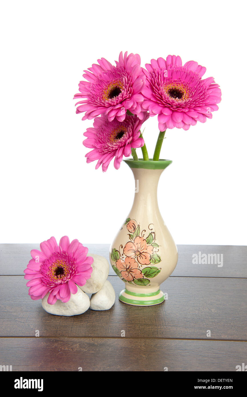 Gerbera rose en vase décoré avec des tas de pierres blanches sur une étagère en bois brun foncé Banque D'Images