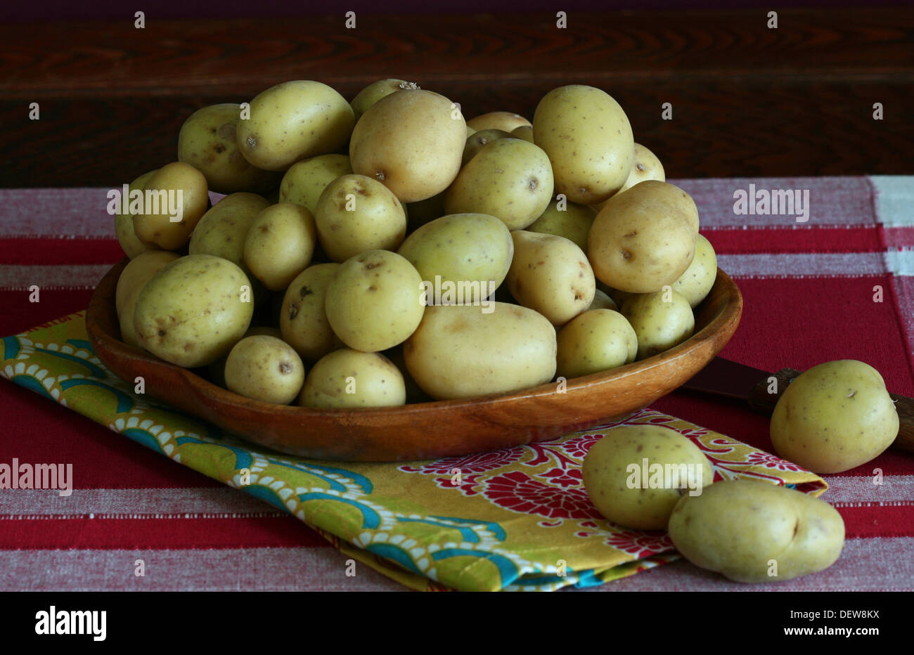 Tas de petites pommes de terre jaunes dans un bol en bois sur une place rouge et blanc mat. Banque D'Images