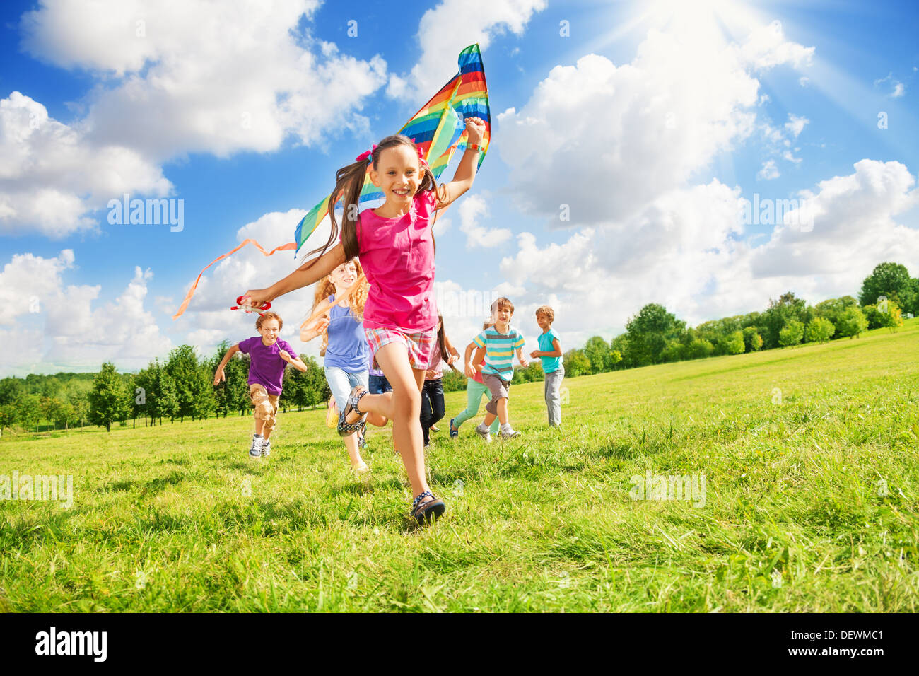 Happy cute smiling girl exécuter avec cerf-volant et d'autres enfants garçons et filles exécutant ensemble dans le parc aux beaux jours Banque D'Images