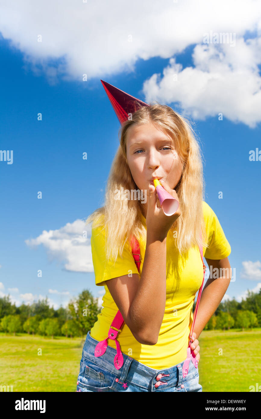 Belle petite fille soufflant dans crécelle et corne d'anniversaire à l'extérieur de la pac avec l'expression heureuse sur journée ensoleillée Banque D'Images