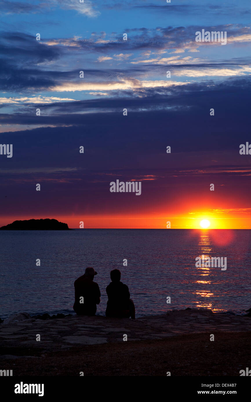 Couple en regardant le soleil tomber dans la mer au coucher du soleil Banque D'Images