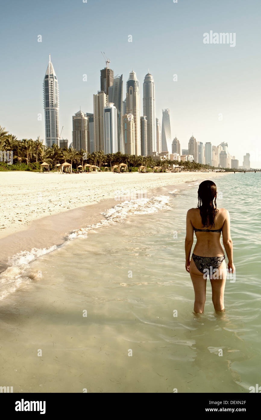 Femme sur la plage en regardant vers les gratte-ciel modernes formant l'horizon de Dubaï en Émirats Arabes Unis Banque D'Images