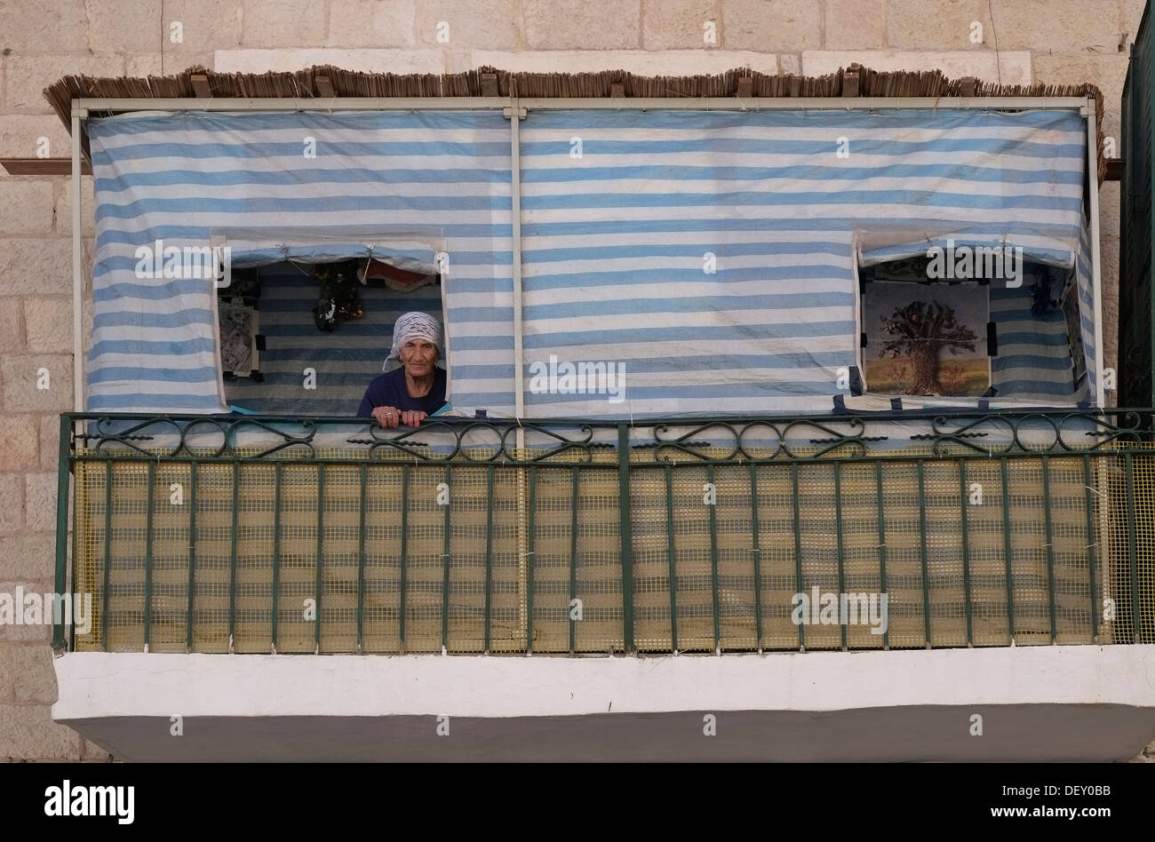 Une vieille femme juive piaulements d'une Soucca traditionnels ou succah hut érigée sur un le balcon de sa maison pendant la semaine de fête de Souccot juif à Jérusalem Israël Banque D'Images