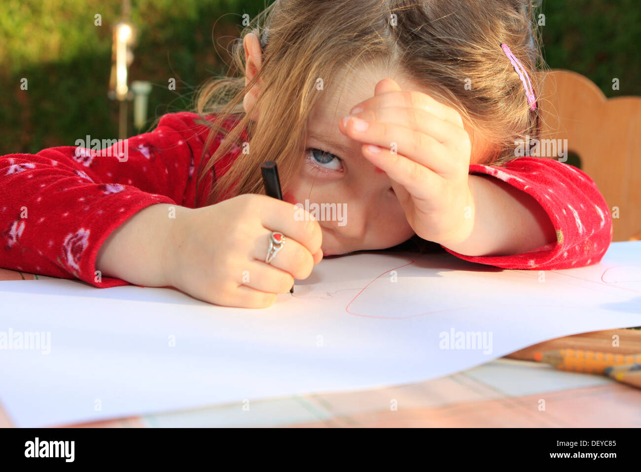 Petite fille, trois ans, la peinture avec un stylo sur une feuille blanche, assis à une table Banque D'Images