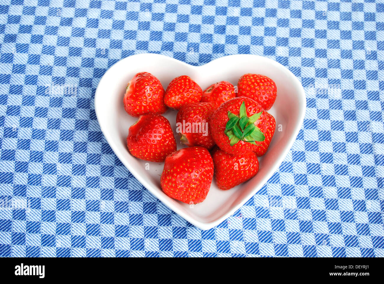 Les fraises, le bol en forme de coeur en porcelaine, nappe à carreaux Banque D'Images