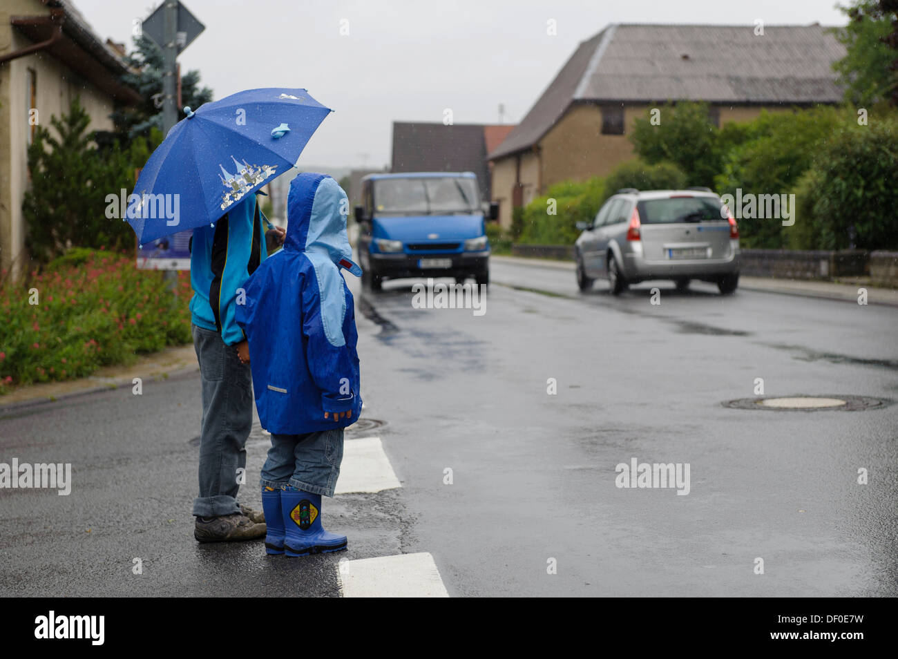Deux enfants, 4 et 8 ans, en attendant de traverser la rue sous la pluie, deux voitures, Assamstadt, Bade-Wurtemberg Banque D'Images