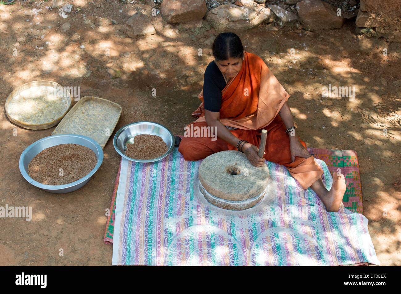 Femme village à l'aide de meules pierres pour moudre le mil rouge / Graines Graines Ragi Ragi en farine. L'Andhra Pradesh. L'Inde Banque D'Images